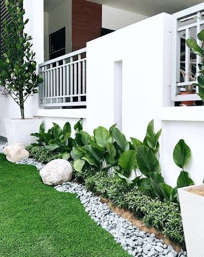 Front-of-house foundation planting with tropical foliage, white pebble border and artificial lawn, by GP FloraL