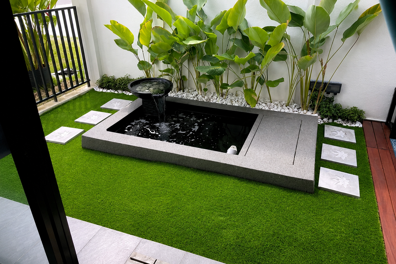 Modern granite-edged garden pond with a spillway bowl, water plants and stepping stones on artificial lawn, built by GP FloraL