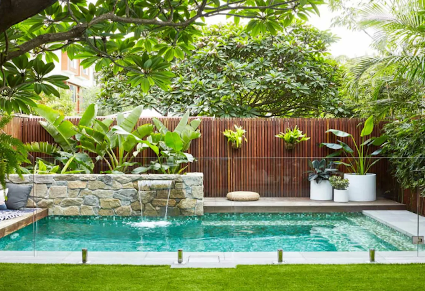 Resort poolside tropical landscape with stone water feature, timber screen and lush planting, by GP FloraL