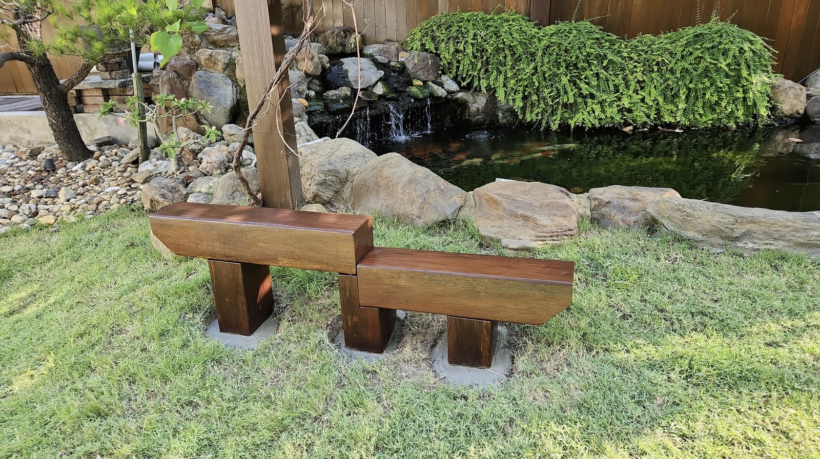Timber bench beside a koi pond and rock waterfall, built by GP FloraL